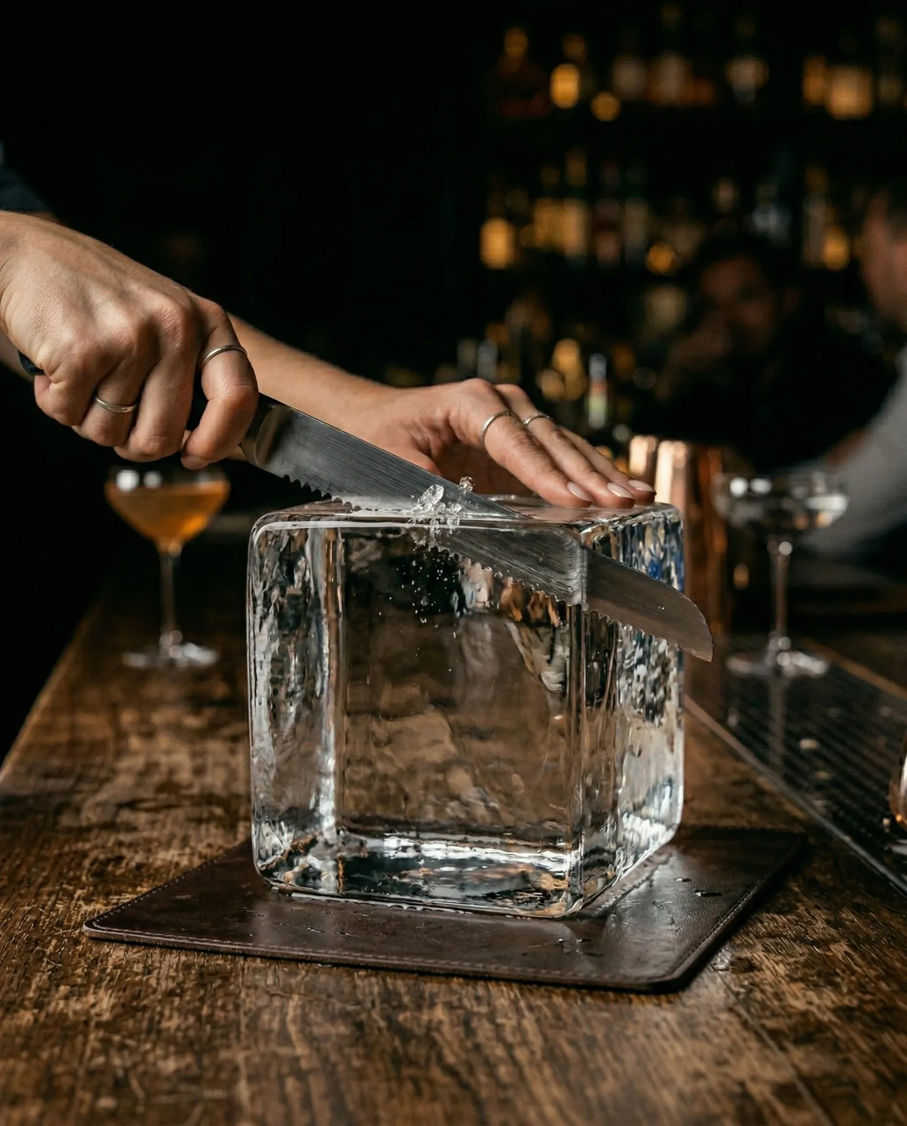 A serrated knife and wooden mallet being used to score a clear ice block into cubes