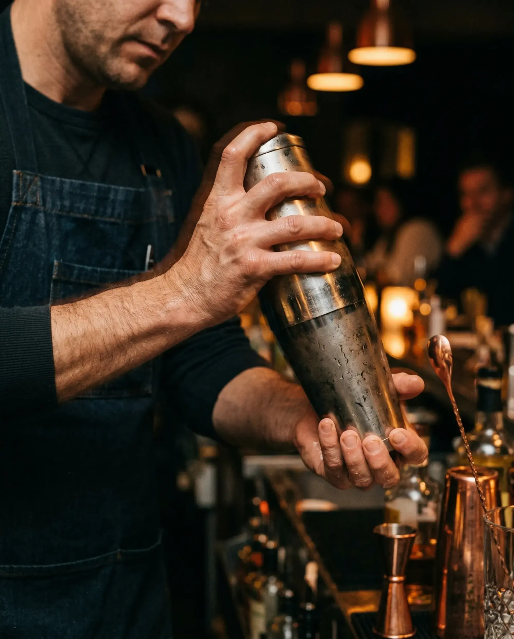 A bartender shaking a metal cocktail tin behind a wooden bar